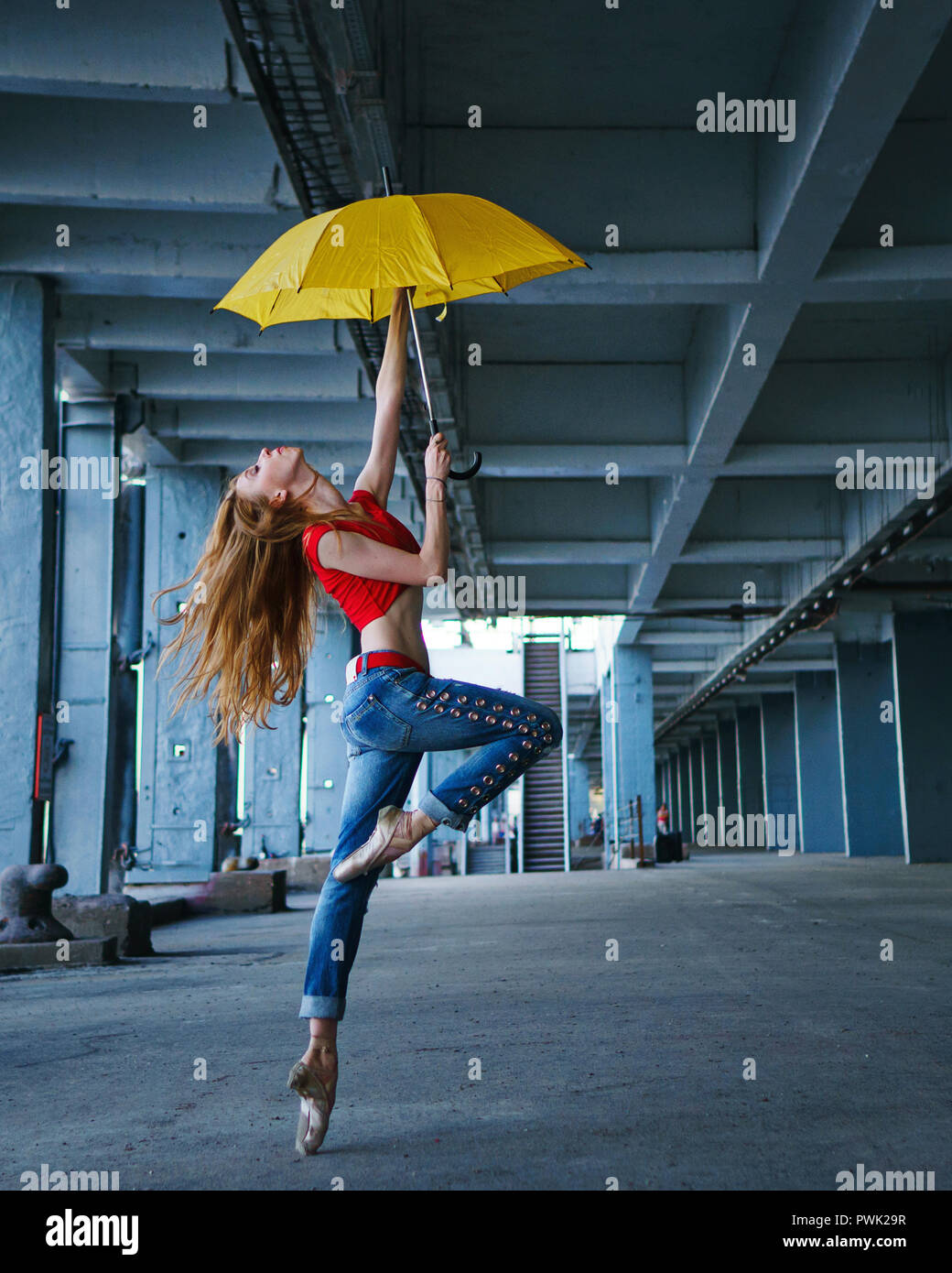 Ballerine danse avec un parapluie jaune en jeans, T-shirt et pointe. La  performance de la rue. Ballet moderne. Slim girl dancing sur la pointe des  pieds. Les cheveux rouges fly Photo Stock -