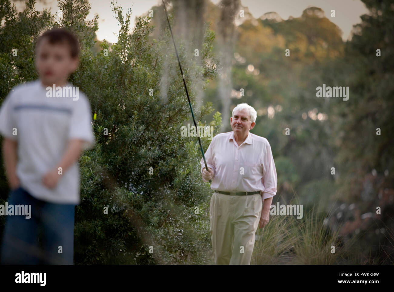 Senior homme marchant à travers la garrigue, porteur d'une canne à pêche avec son jeune petit-fils. Banque D'Images