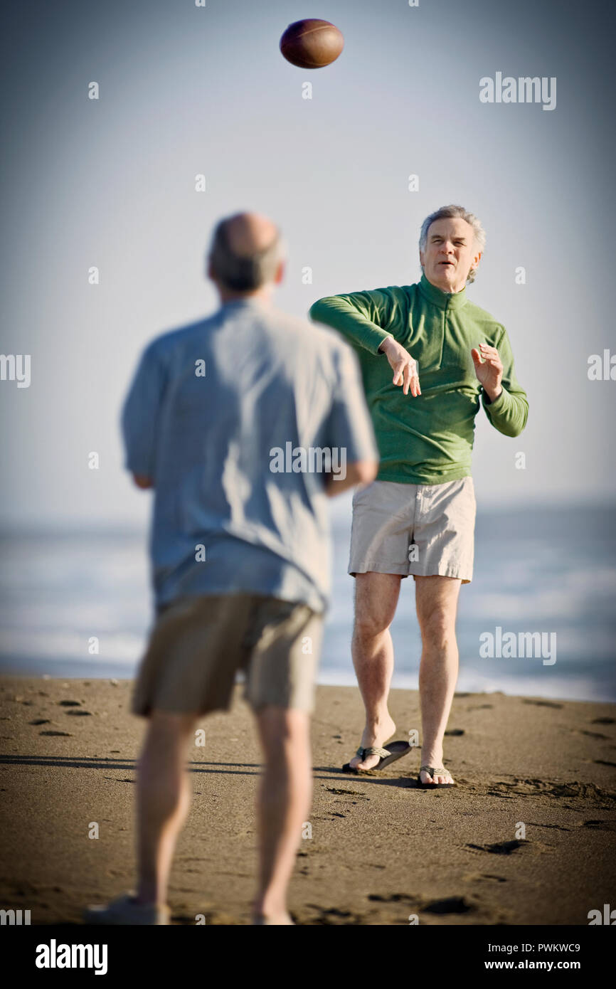 Man throwing a football avec un ami sur une plage de sable. Banque D'Images
