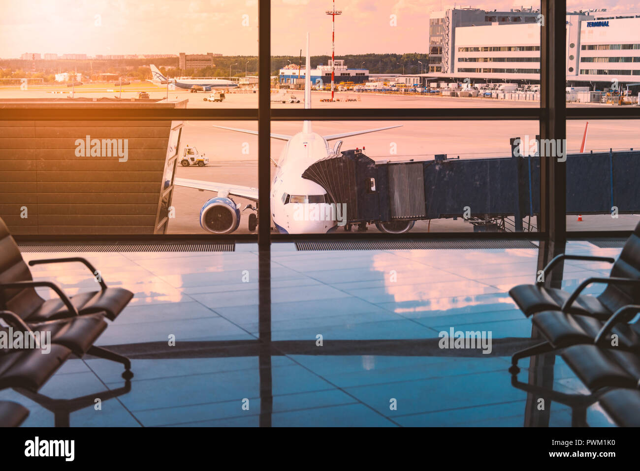 Rangées de sièges vides en zone d'attente de l'aéroport. Chaises en grand hall lumineux attendent des passagers à l'arrivée. Voyages et déplacements. Avion en arrière-plan Banque D'Images