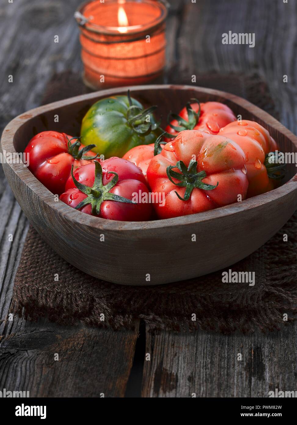 Les tomates dans un bol en bois en face d'une bougie Banque D'Images