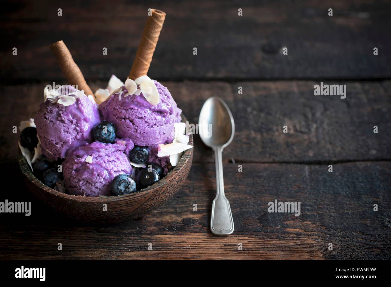 Boules de glace à la myrtille surmonté d'amandes effilées et le chocolat gaufre bobines dans un bol en bois Banque D'Images