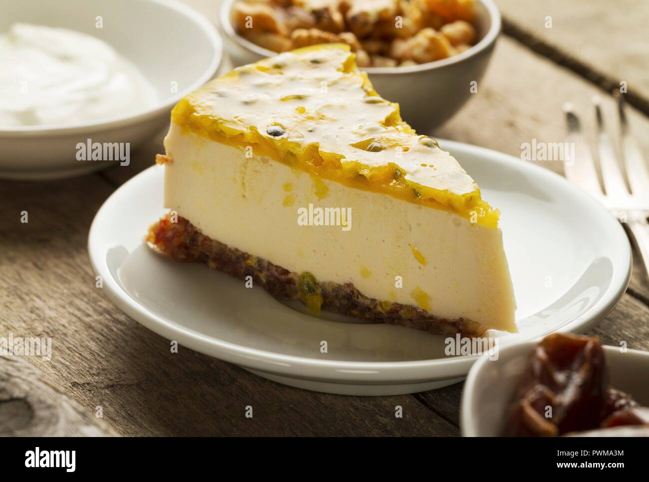 Une tranche de gâteau au yaourt grec et au mascarpone avec une date et une base de noix, garni de maracuja Banque D'Images