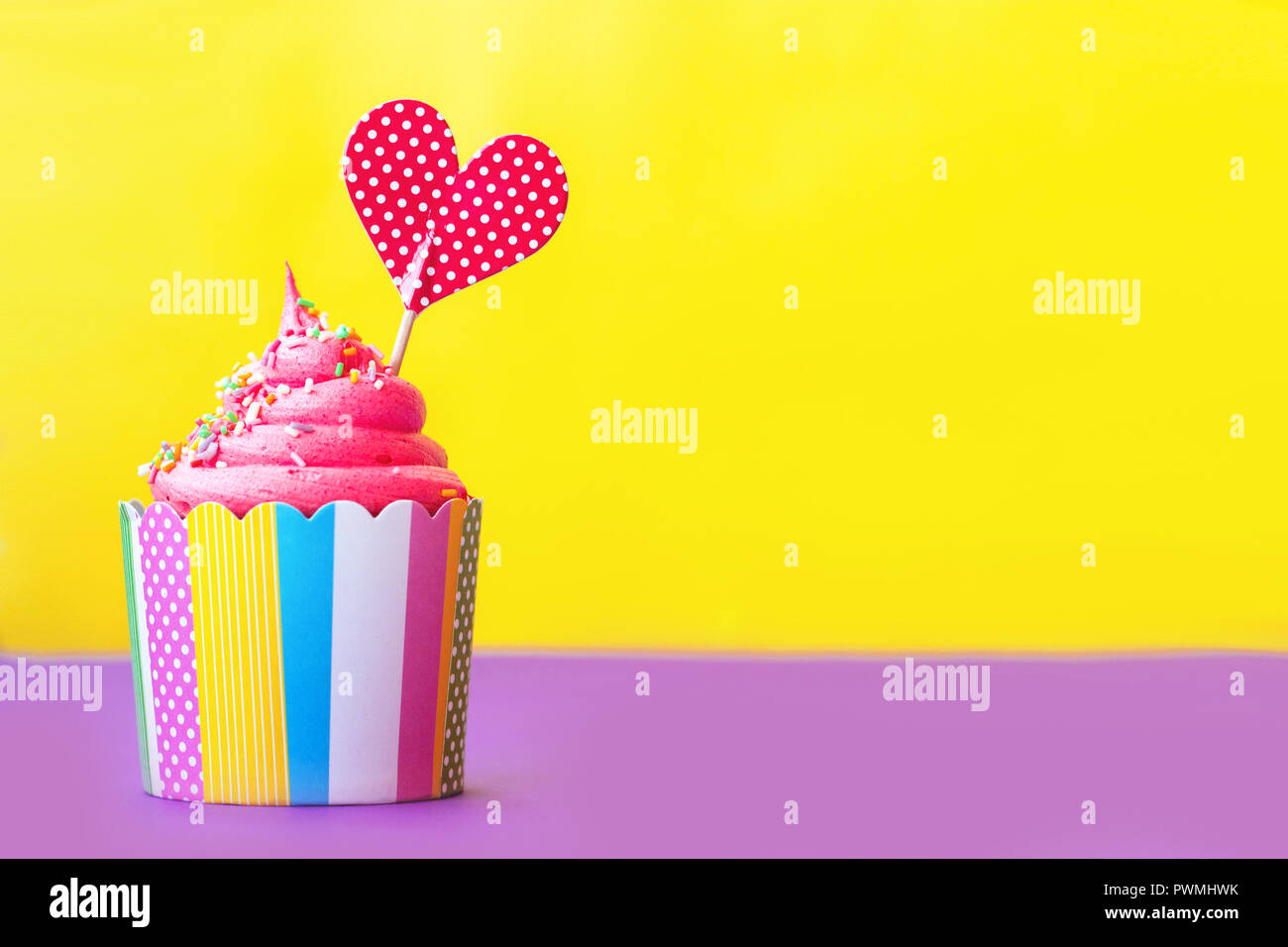 Cupcake fraise savoureuse dans du papier coloré, de la coupe de cuisson avec surmatelas, coeur rouge sur fond jaune. Partie ou valentines background Banque D'Images