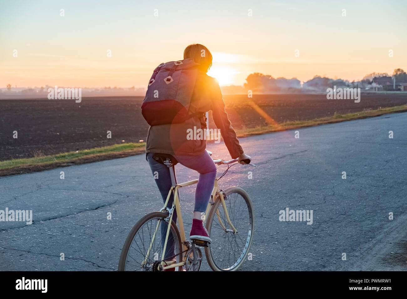 Femme commuter le vélo de la ville pour la banlieue. Femme à vélo le long de la route au coucher du soleil Banque D'Images