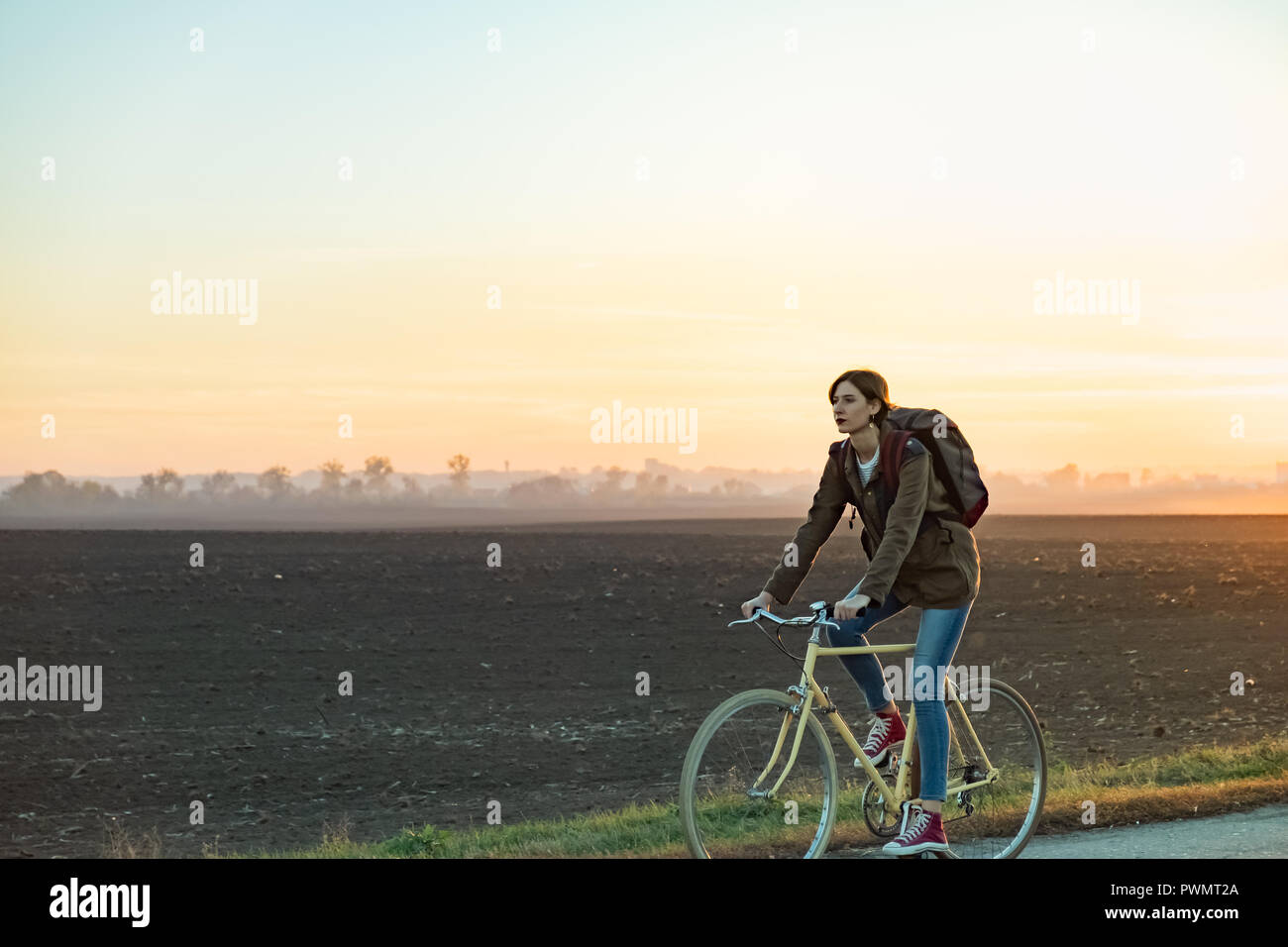 Circonscription de banlieue femelle un vélo à l'extérieur de la ville en zone rurale. Young woman riding bike au coucher du soleil Banque D'Images