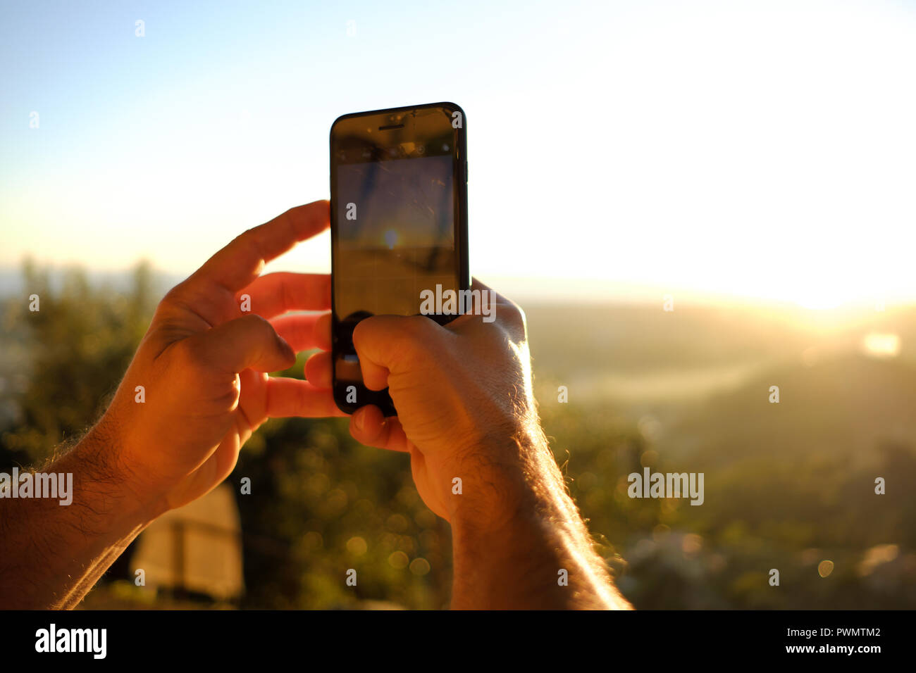 Mains homme baignée de soleil en prenant une photo avec téléphone cellulaire Banque D'Images