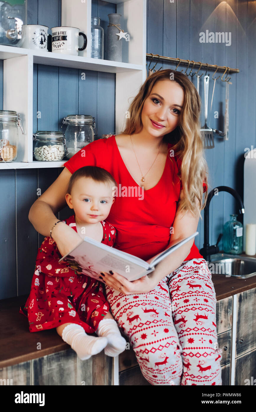 Belle blonde avec mère fille assis ensemble à la cuisine en pyjama et  souriant. Petite fille avec maman portant des pyjamas de Noël re Photo  Stock - Alamy