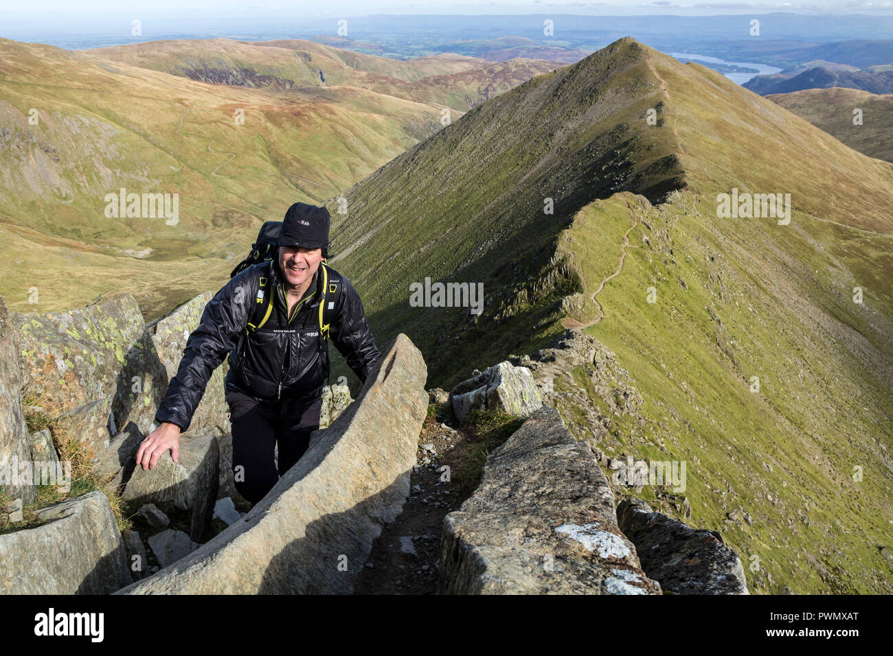 Walker Scrambling sur Swirral Edge avec la montagne de Catstye Cam dans l'arrière-plan, Helvellyn, Lake District, Cumbria, Royaume-Uni. Banque D'Images