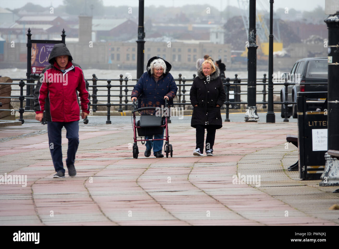 Météo britannique. Une femme marchant le long de la promenade avec une aide à la mobilité en cas de tempête Banque D'Images