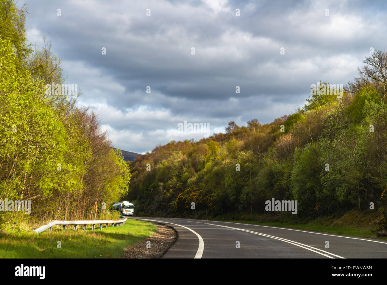 Une route sinueuse à travers une forêt de nuages gris au-dessus. chariot dans la distance. Banque D'Images