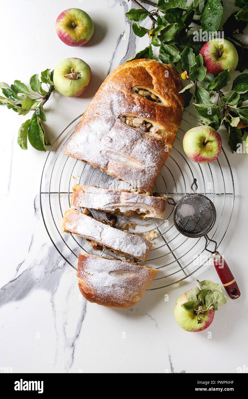 Des tranches de pâte feuilletée strudel aux pommes Tarte sur grille de refroidissement servi avec des pommes mûres, branches, cieve et le sucre en poudre sur le marbre blanc textur Banque D'Images