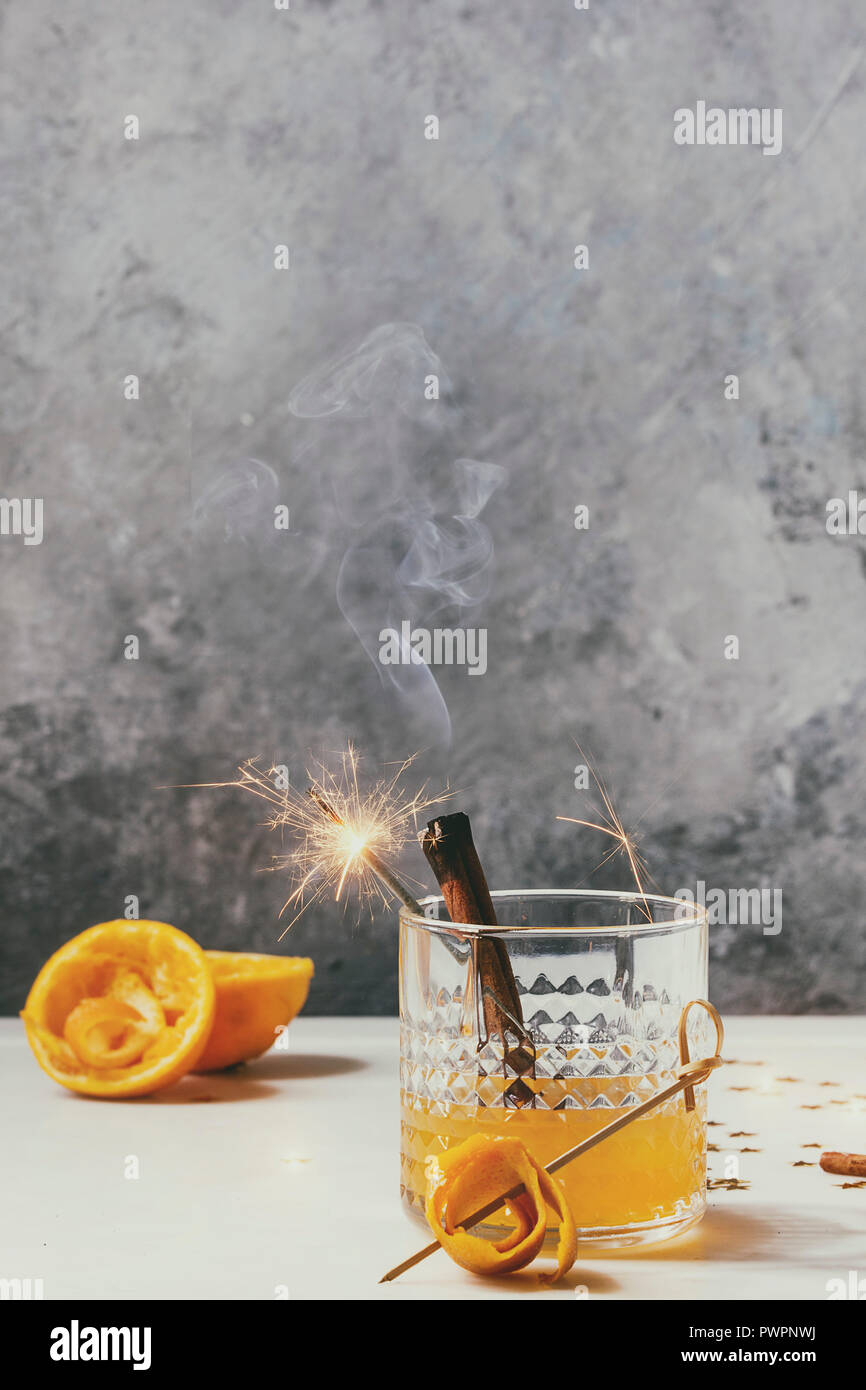 Verre de jus d'orange Whisky cocktail avec alcool tourbillonnait d'orange et bâtons de cannelle fumeurs debout sur la table en marbre blanc avec golden Banque D'Images