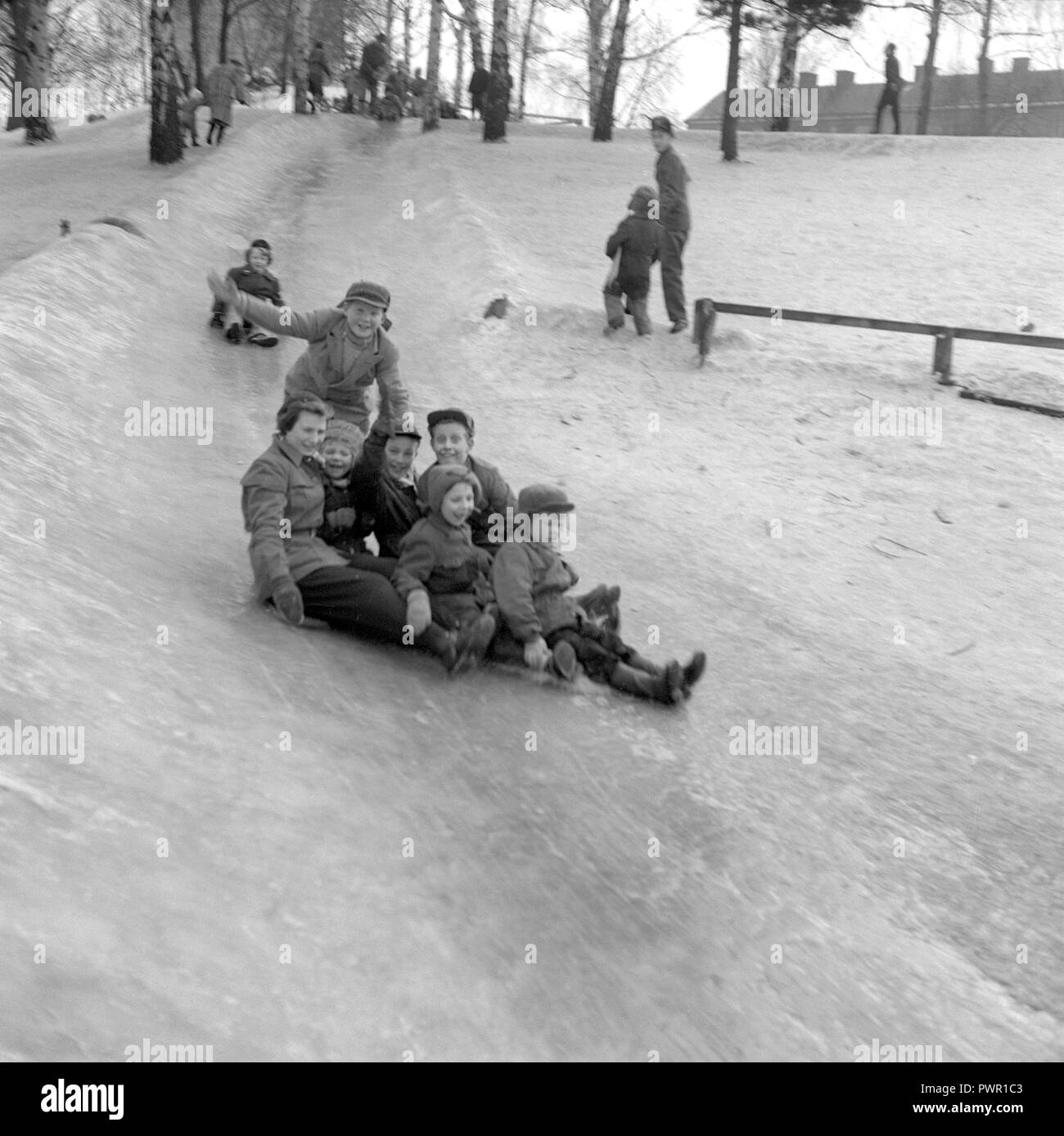 L'hiver dans les années 1950. Des enfants jouent dans un parc à Stockholm. Le glisser sur la colline glacée ensemble et avoir du plaisir. Suède 1951. Ref 1609 Banque D'Images