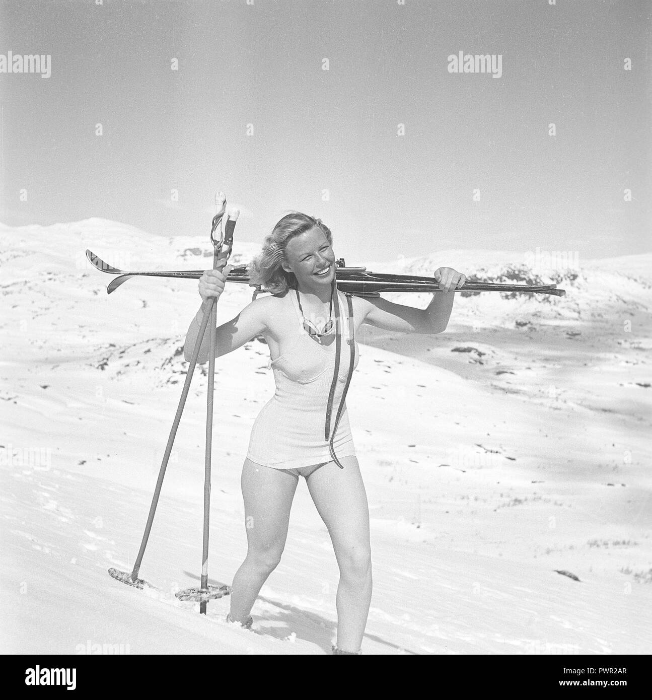 L'hiver dans les années 40. Une jeune blonde femme suédoise est transporter ses skis sur l'épaule, marchant dans la neige profonde sur le sommet d'une montagne. Elle porte un maillot de bain et jouit de la journée ensoleillée. La Suède des années 40. Kristoffersson Photo ref H139-6 Banque D'Images
