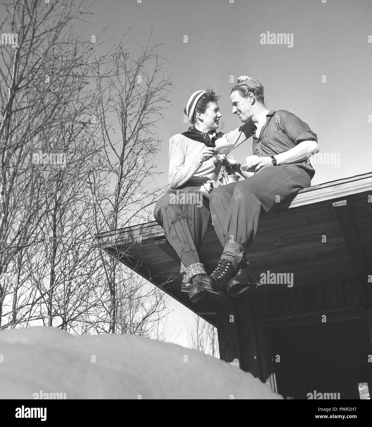 L'hiver dans les années 40. Un jeune couple est d'avoir une tasse de café, assis sur le toit de leur maison. La Suède des années 40. Kristoffersson Photo Ref D1-9 Banque D'Images