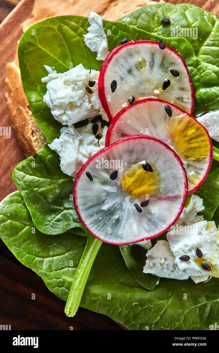 Sandwichs sains lumière avec du pain toasts, fromage doux et des radis, des épinards biologiques recueillies sur une planche de bois. Close-up Banque D'Images