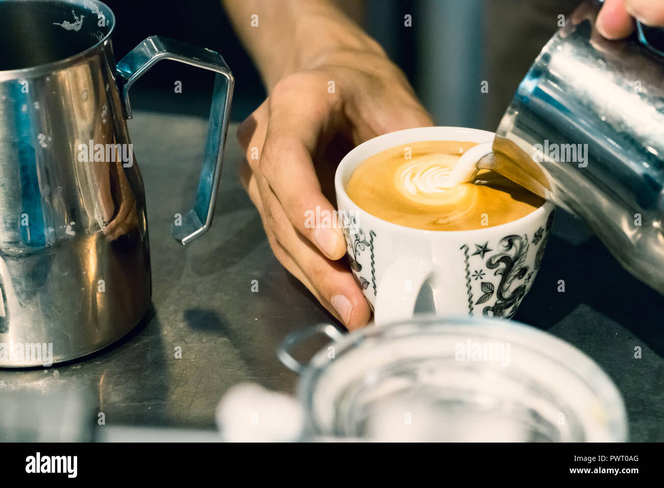 Close-up d'un barista pouring hot mâles mains mousse de lait sur une tasse de Latte art cappuccino. Banque D'Images