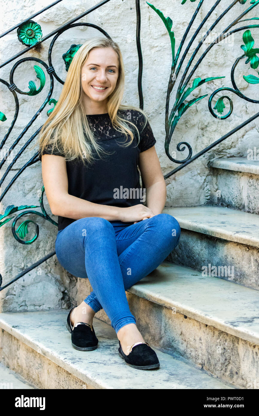 Portrait d'une jeune femme blonde en Pologne, 24 ans, assis sur des escaliers en marbre, à huis clos, souriant, heureux à l'extérieur. Banque D'Images