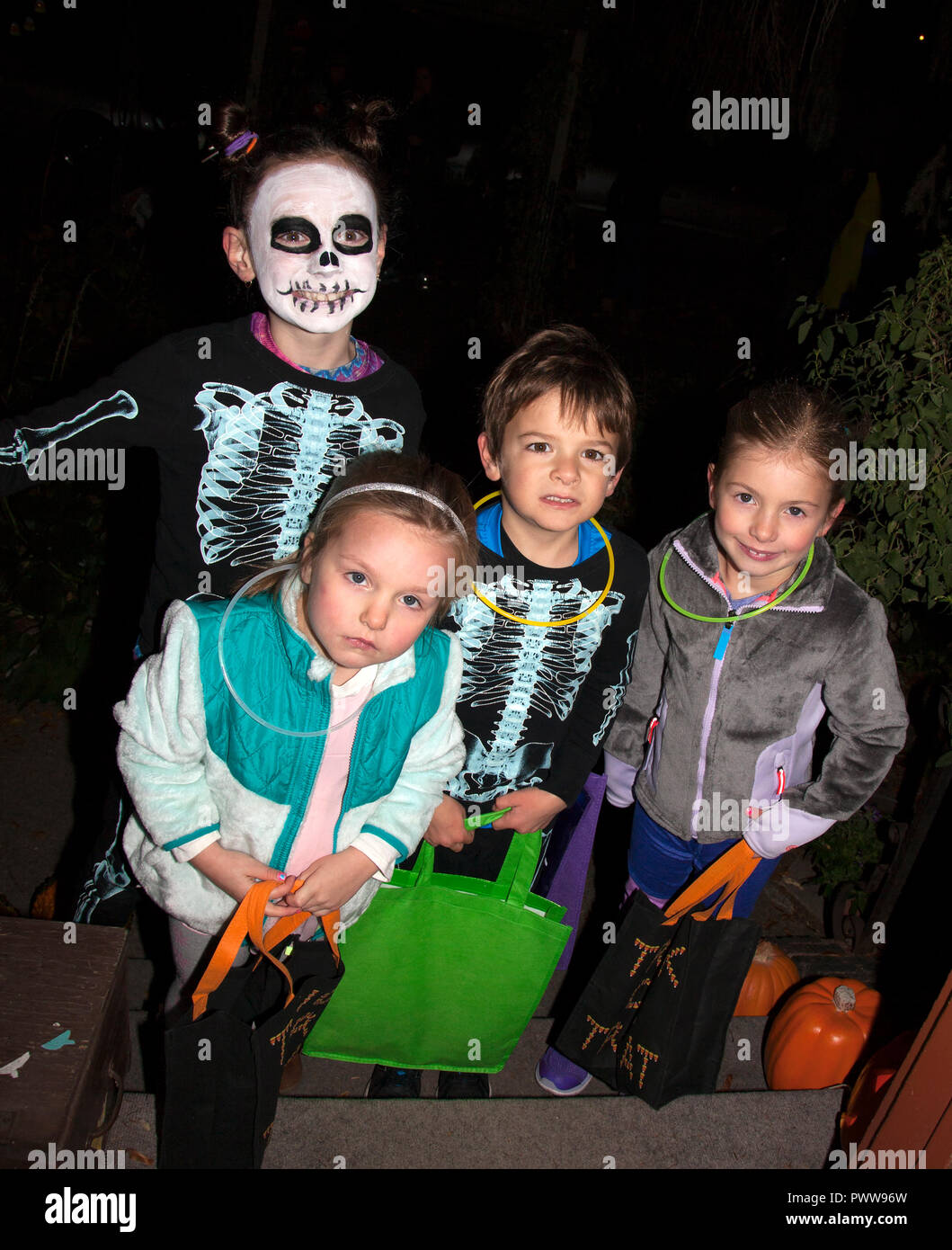 Ressemble à quatre frères et sœurs dehors pour une nuit de Halloween trucs ou traite avec les deux plus anciens vêtus de costumes squelette. St Paul Minnesota MN USA Banque D'Images