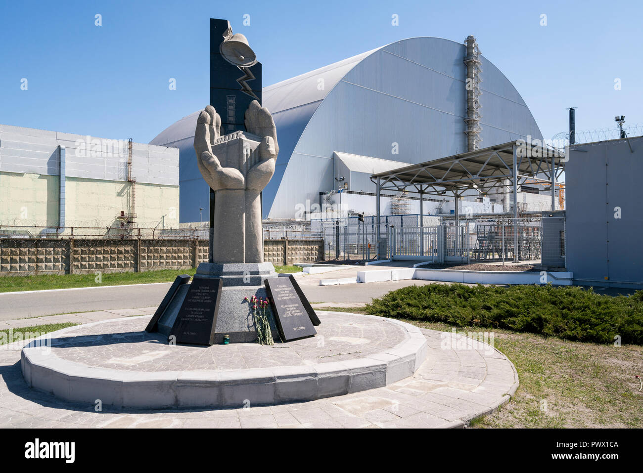 Des fleurs au monument devant le sarcophage, la structure d'acier et de béton couvrant le réacteur nucléaire n° 4 à Tchernobyl, en Ukraine. Banque D'Images