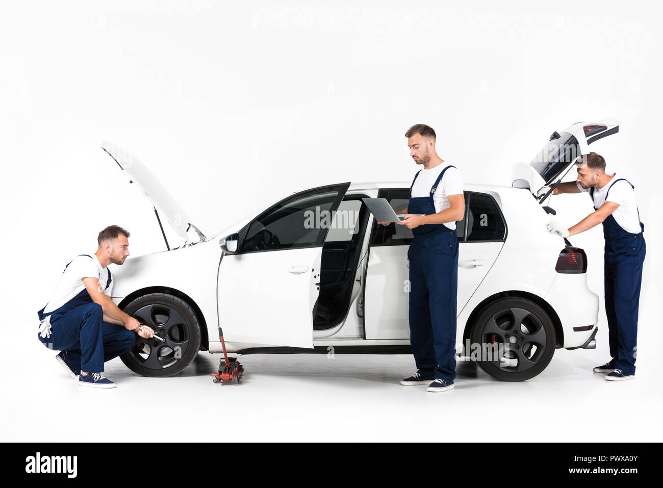 Mécanicien auto changement de pneu de voiture, à l'aide d'ordinateur portable et à en ouvrir coffre de voiture on white Banque D'Images
