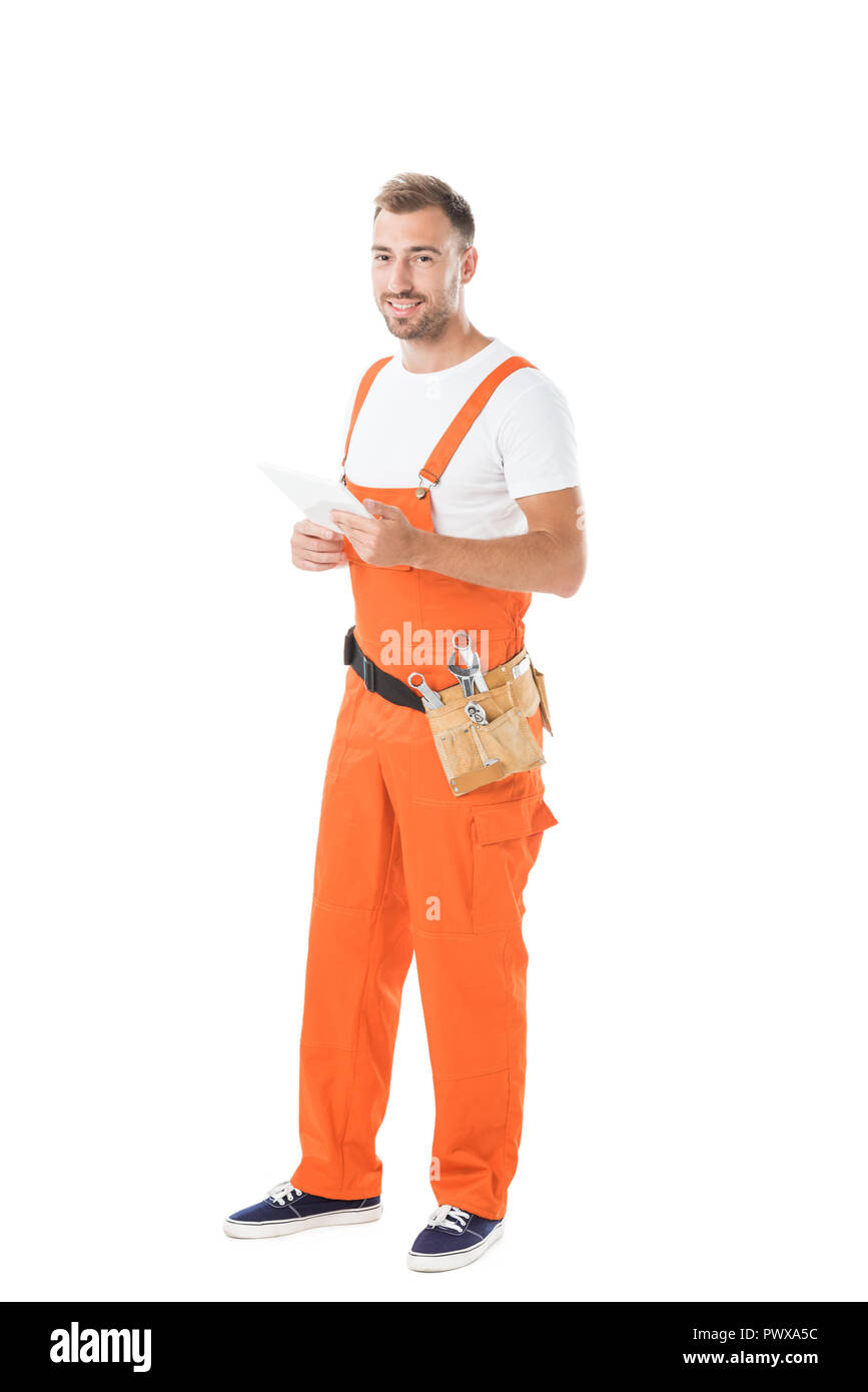 Smiling handsome auto mechanic en uniforme orange holding tablet isolated on white Banque D'Images