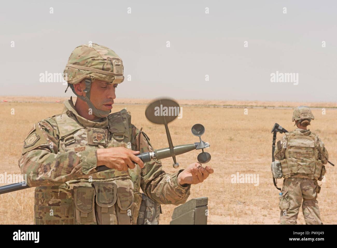 Le sergent-chef de l'US Air Force. Scott, le flexible de la météo NCOIC affecté à la 370e groupe consultatif expéditionnaire aérienne, le détachement 1, effectue une inspection de maintenance préventive sur un capteur météo tandis que le sergent-chef. Shannon Hawkins effectue de la zone de sécurité à Qayyarah Aérodrome de l'Ouest, de l'Iraq, le 2 juillet 2017. Scott et son frère Master Sgt. Daniel flexible sont déployés à l'Iraq à l'appui de la Force Opérationnelle Interarmées -Fonctionnement résoudre inhérent. Les GFIM-OIR est la Coalition mondiale pour vaincre ISIS en Iraq et en Syrie. Banque D'Images