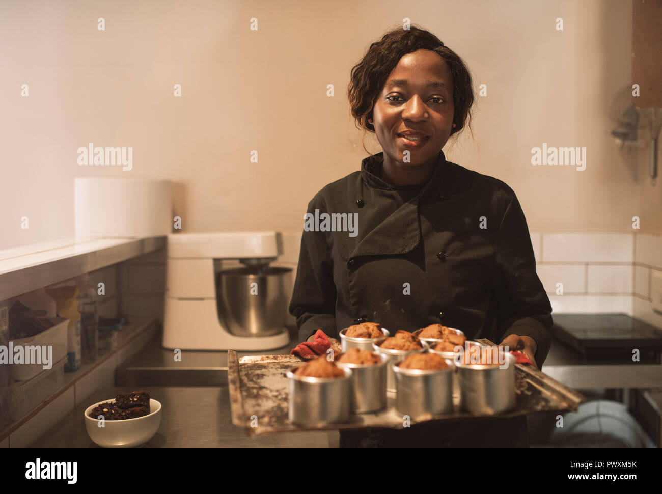 Smiling baker holding a tray de muffins dans sa cuisine Banque D'Images