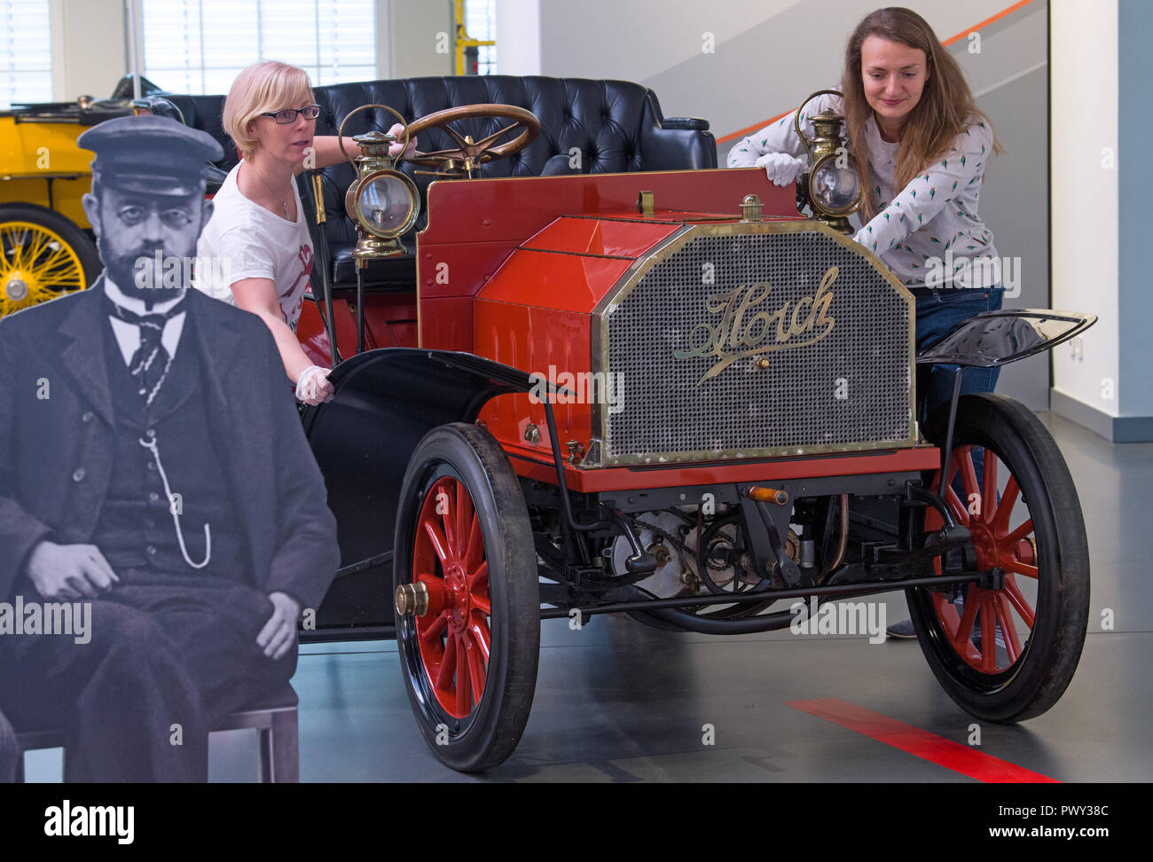 18 octobre 2018, Saxe, Zwickau : Deux employés de la Musée Août Horch à Zwickau pousser un "modèle Horch 2' avec 12 ch en position à côté d'un portrait d'August Horch (l). Le musée de l'automobile a une exposition spéciale commémorant le 150e anniversaire de son homonyme. Le spectacle retrace la vie de l'ingénieur, né à Winningen le 12 octobre 1868, à partir de son enfance jusqu'à sa mort en 1951. Horch fonde son usine automobile à Zwickau en 1904. L'exposition peut être vu du 20 octobre au 27 janvier 2019. Photo : Hendrik Schmidt/dpa-Zentralbild/dpa Banque D'Images
