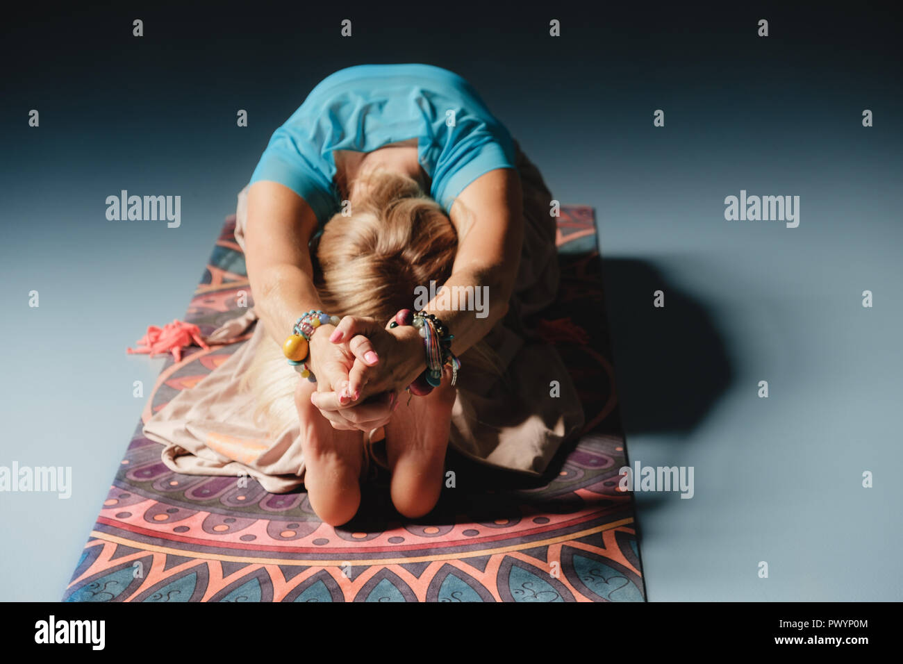 Une belle femme mature blonde aux yeux bleus de faire le yoga à l'intérieur seul dans des vêtements colorés et accessoires. Banque D'Images