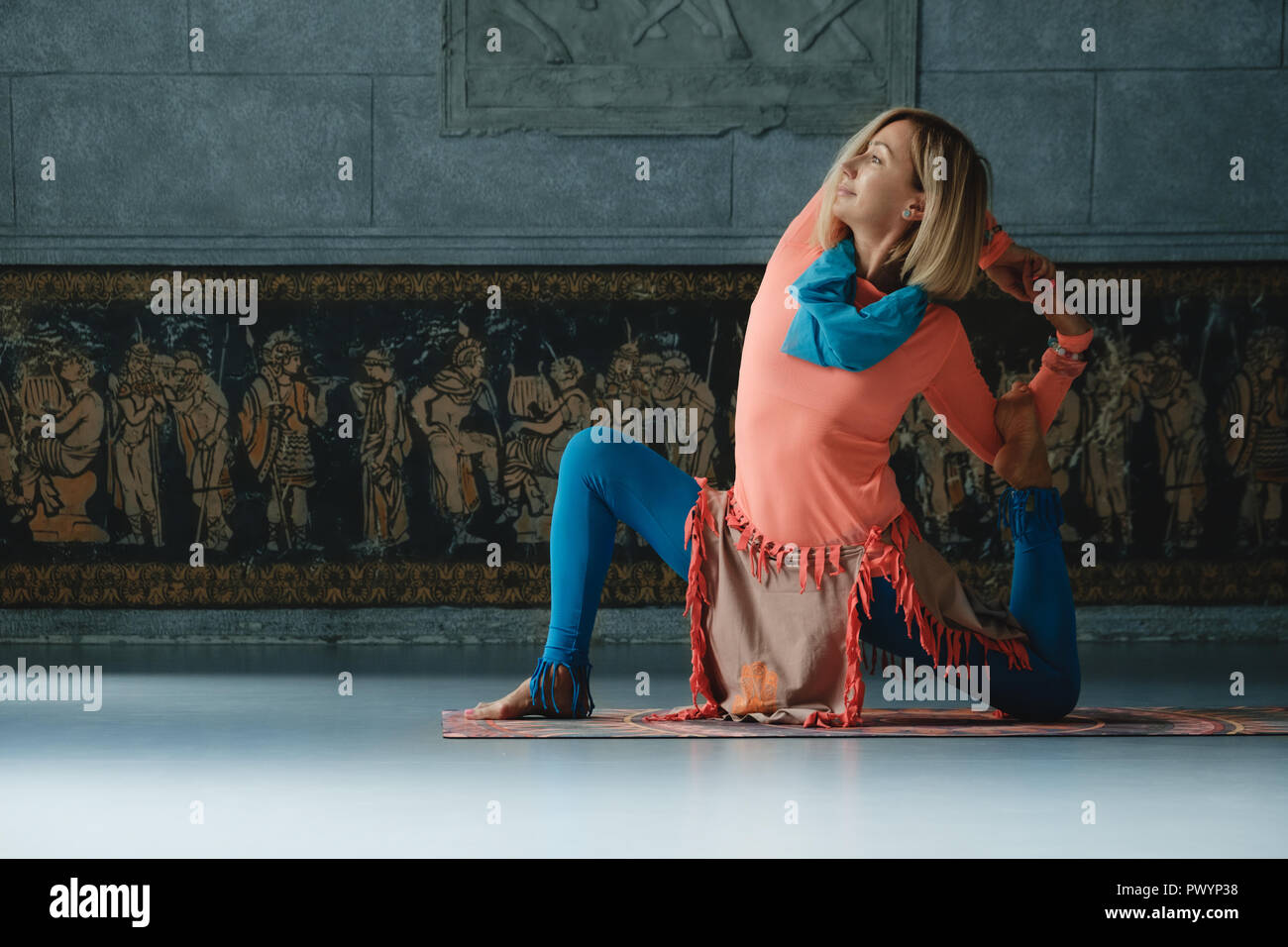 Une belle femme mature blonde aux yeux bleus de faire le yoga à l'intérieur seul dans des vêtements colorés et accessoires. Banque D'Images