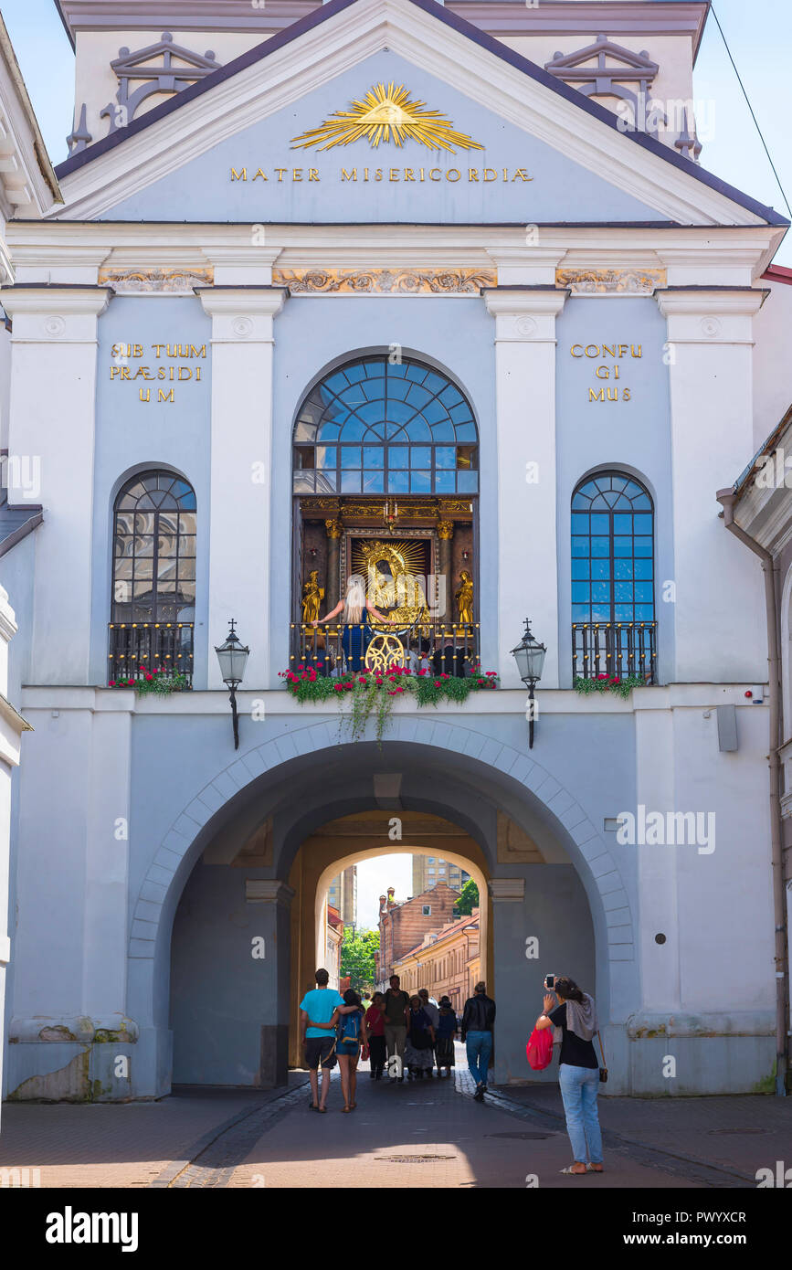 Chapelle de la porte de l'Aurore, dans la vieille ville de Vilnius une  femme prend une photo de personnes qui visitent la chapelle et sanctuaire  de la Madonna de la porte de