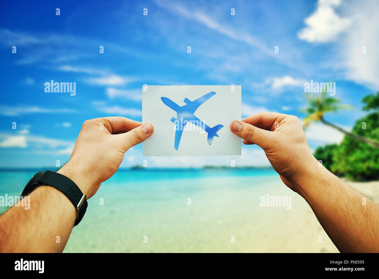 Close up of man mains tenant une feuille de papier blanc avec l'icône avion sur fond de plage tropicale avec la mer bleue, ciel clair et de palmiers exotiques. Lo Banque D'Images