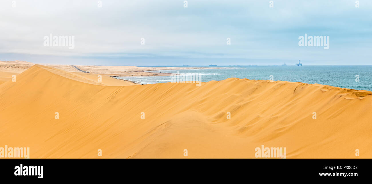 Dune de sable jaune longue de désert du Kalahari et océan Atlantique côte, avec des plates-formes pétrolières et les navires à l'horizon, à proximité de la ville de Swakopmund, Namibie Banque D'Images