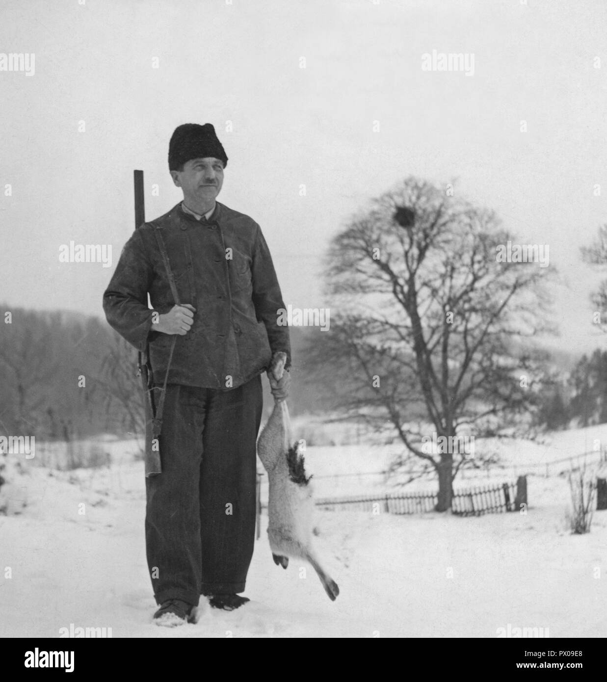 Hunter dans les années 40. Un homme est debout et tenant un lièvre qu'il a tourné lors de la chasse pour le lièvre traditionnel de Noël. Une tradition en décembre et souvent proche de noël. Suède 1940 Banque D'Images