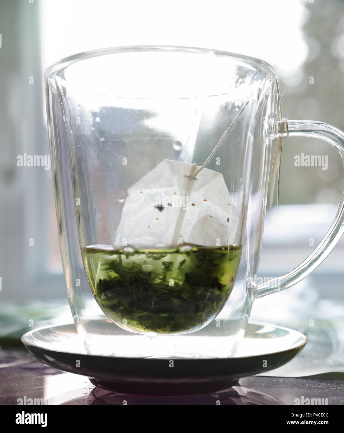 Dans une tasse en verre clair, l'un verse de l'eau chaude sur un sachet de thé vert. Banque D'Images