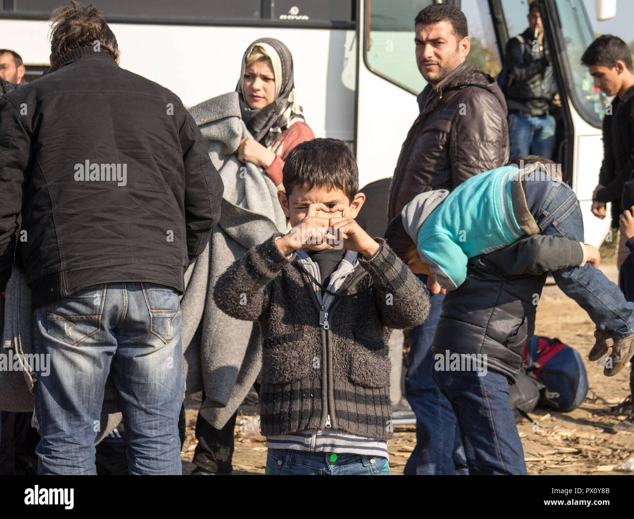 BERKASOVO, SERBIE - 31 octobre 2015 : Jeune garçon, enfant réfugié, souriant et se tenant dans un champ entouré par d'autres réfugiés, près de la Croatie Serbie Banque D'Images