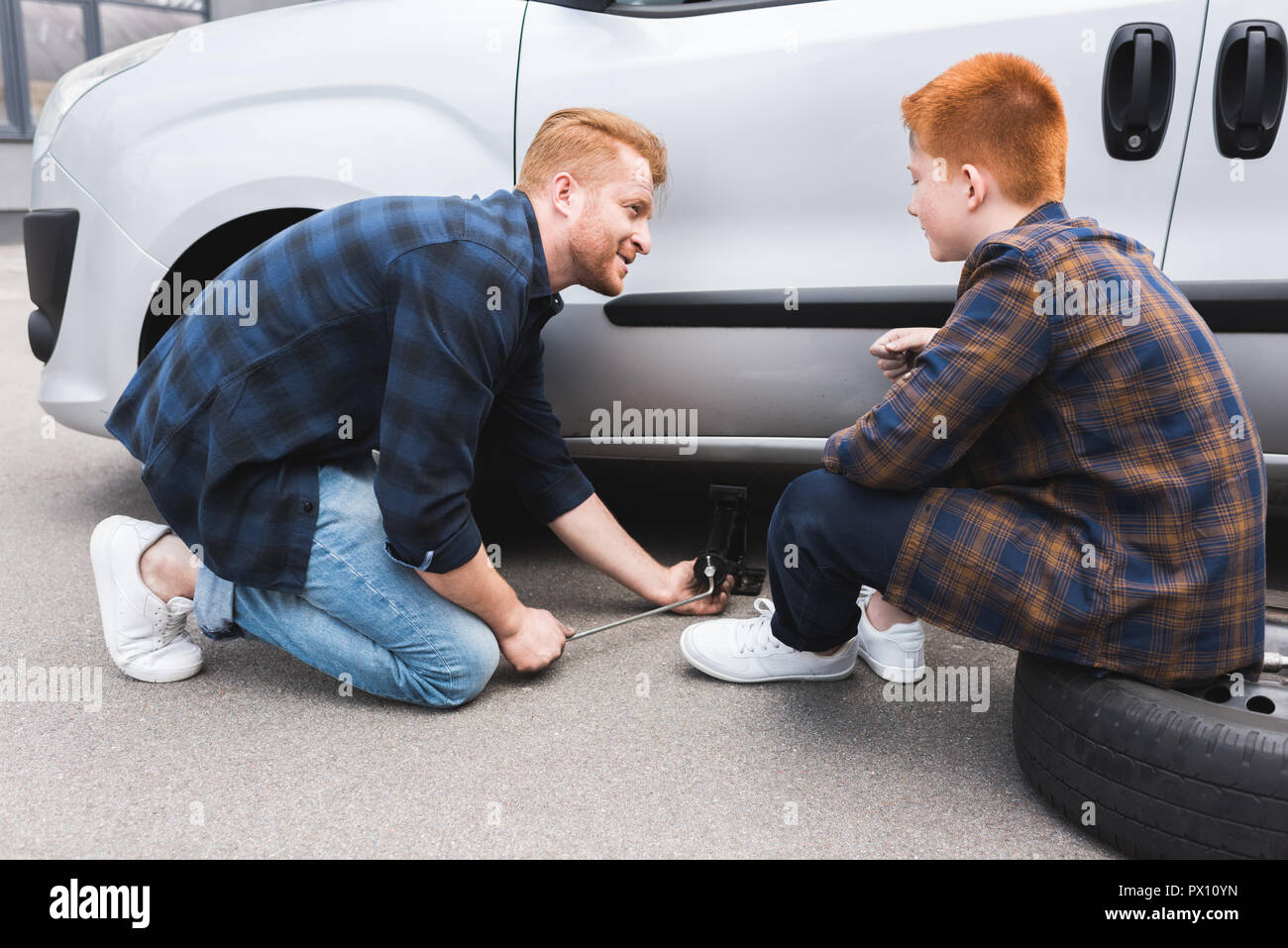 Père avec un cric de voiture de levage pour changement de pneu, fils de le regarder Banque D'Images