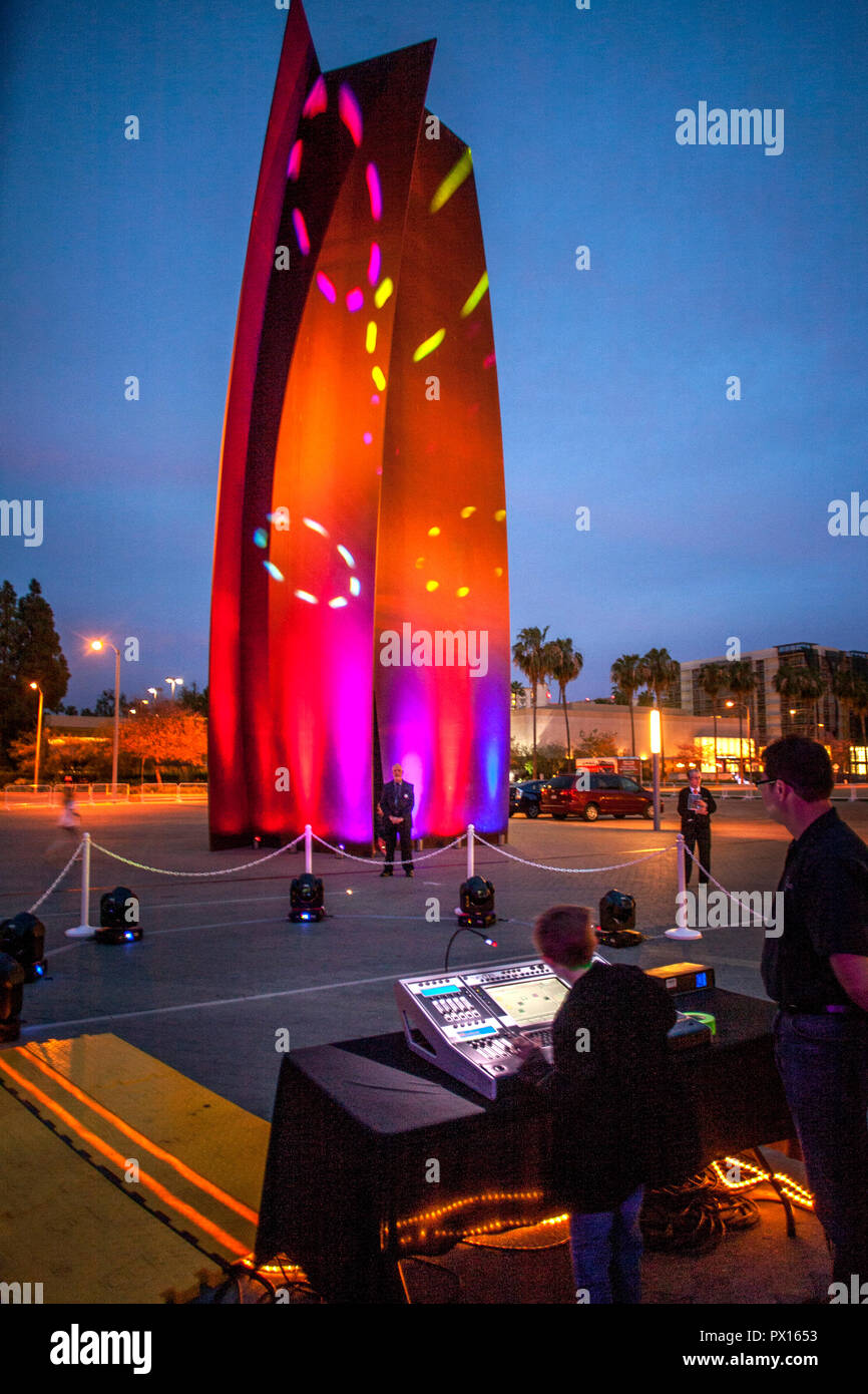 En tant que technicien regarde, un garçon exploite un panneau de lumière laser illuminant d'une sculpture à un festival communautaire de nuit à Costa Mesa, CA. La sculpture, c'est de Richard Serra 'Connecteur.' Banque D'Images