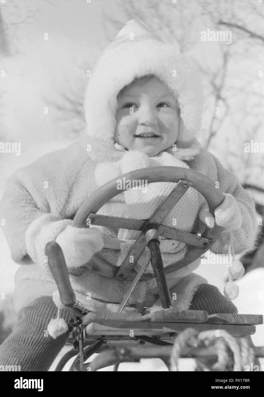 L'hiver dans les années 40. Un enfant est tombé de son traîneau mais ne semble pas à l'esprit. La Suède des années 40. Banque D'Images