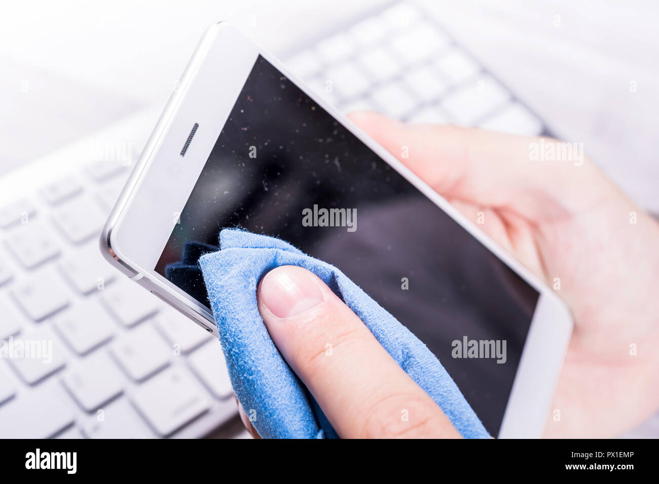 Le nettoyage d'un homme de l'écran du smartphone de la poussière, la saleté et les empreintes digitales avec une lingette de nettoyage à son bureau. Banque D'Images