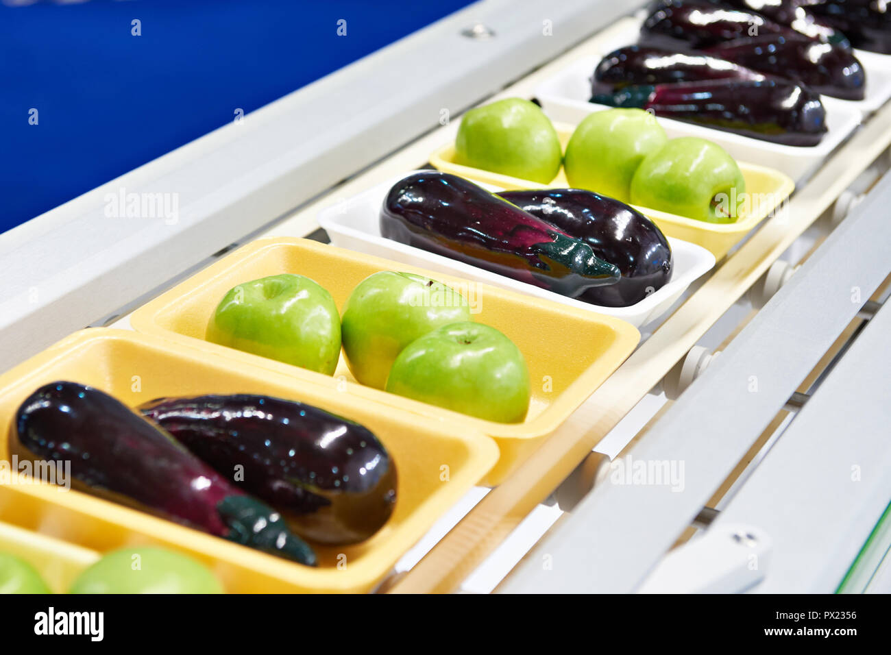 Produits alimentaires les pommes et les aubergines dans l'emballage en plastique sur le convoyeur Banque D'Images