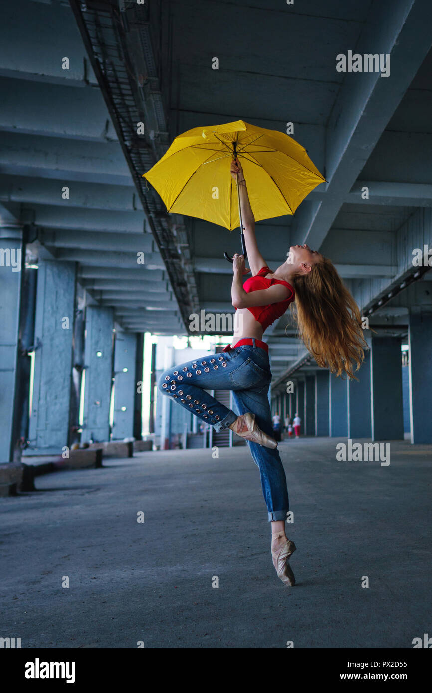 Ballerine danse avec un parapluie jaune en jeans, T-shirt et pointe. La  performance de la rue. Ballet moderne. Fille mince danser sur la pointe des  pieds. Les cheveux rouges fly Photo Stock -