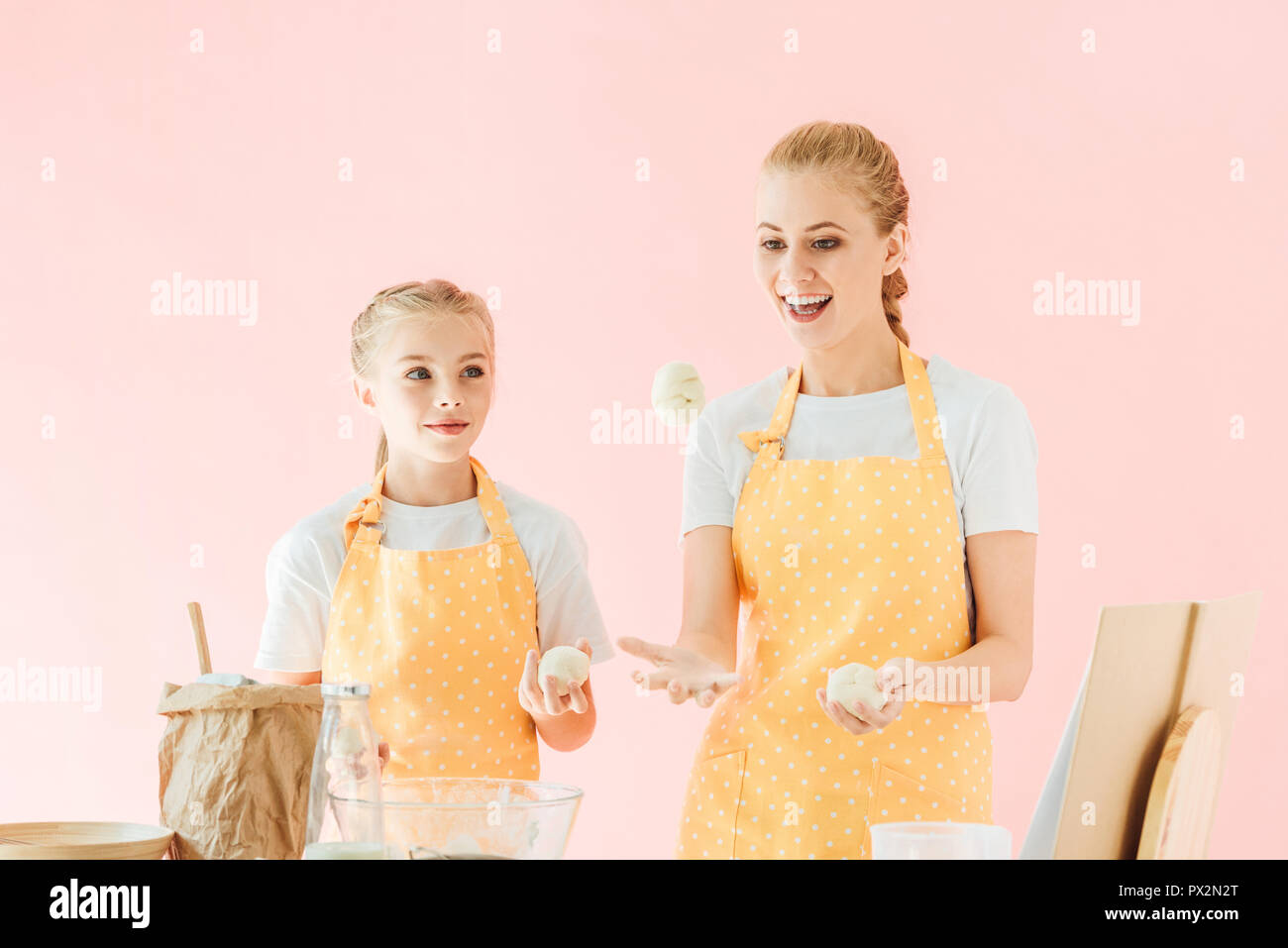 Smiling mother and daughter jonglant avec des morceaux de la pâte pendant la cuisson isolé sur pink Banque D'Images