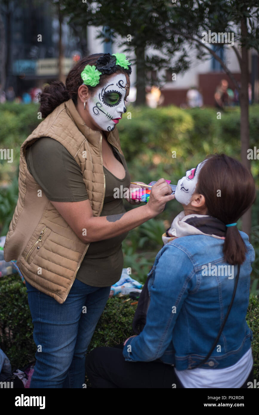 Un artiste de maquillage, le port 'typique' catrina, maquillage met sur le maquillage d'une jeune femme à la traditionnelle Fête des Morts à Mexico City Parade Banque D'Images