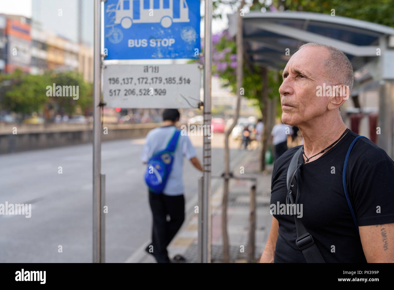 Senior homme chauve touristique pensée lors de l'attente à l'arrêt de bus je Banque D'Images