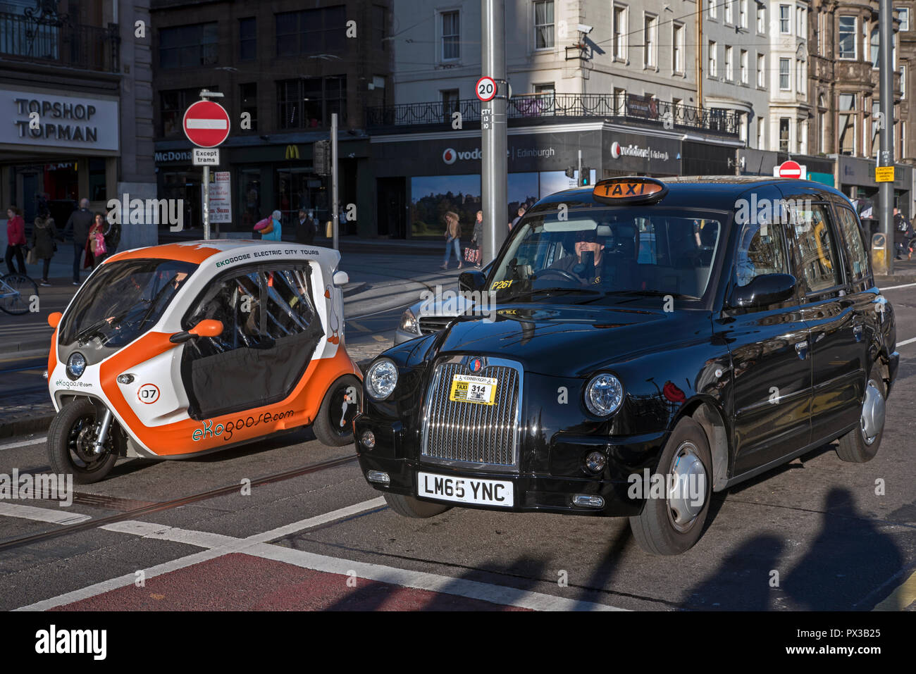 Un eKogoose scooter électrique se trouve à l'phares sur Princes Street à côté d'un taxi. Banque D'Images