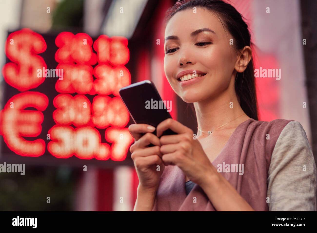 Une belle jeune femme asiatique à l'aide d'une application dans son smart phone pour vérifier les valeurs de change de l'euro et dollar Banque D'Images