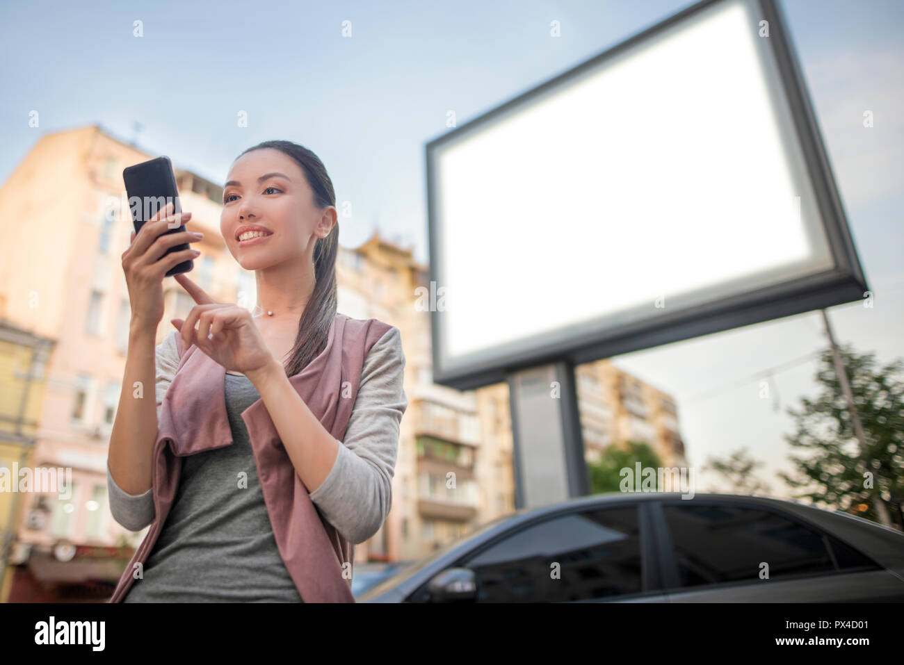 Modèle d'une belle jeune femme asiatique à l'aide d'une application dans son smart phone in front of a blank billboard. Communiquer à l'intérieur de l'espace de copie Banque D'Images